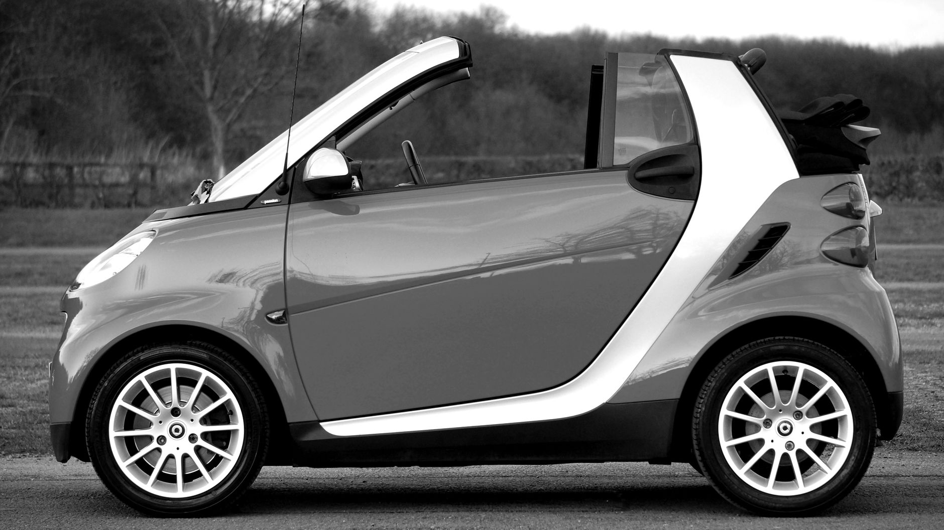 Black and white side view of a stylish Smart convertible car parked outdoors.