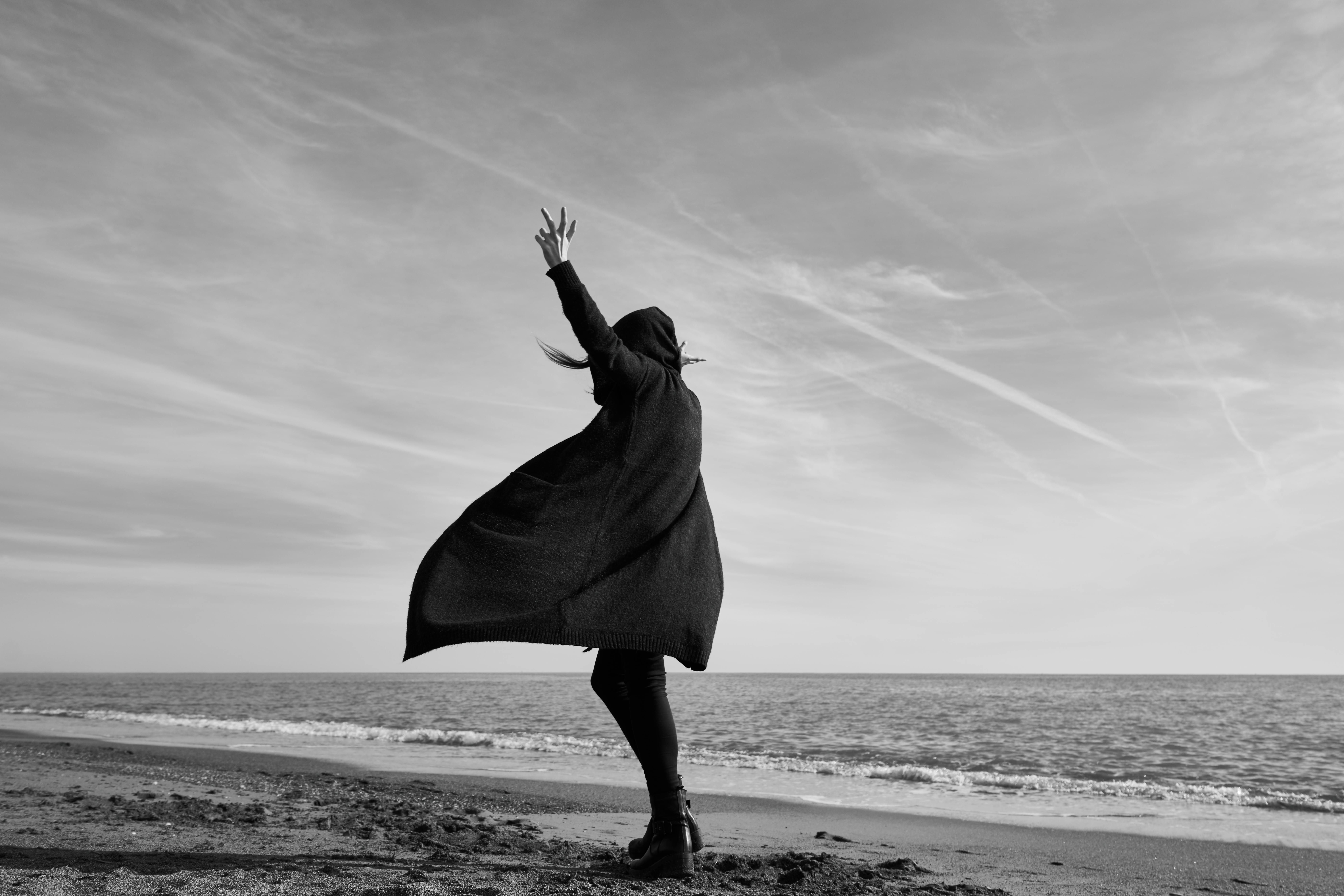 grayscale photography of woman standing on seashore