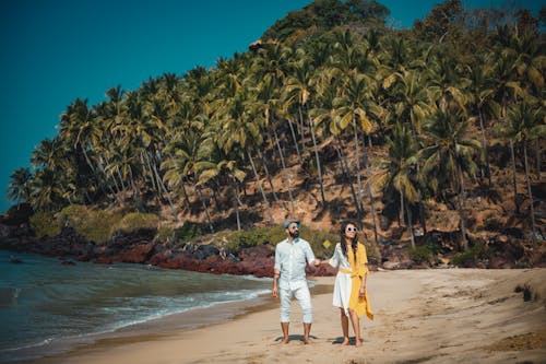 코코넛 나무로 덮인 산 근처 해변에 서있는 남자와 여자