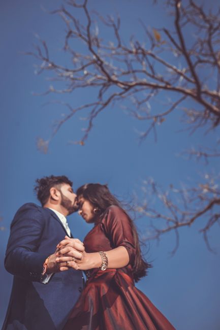 A couple is embracing and holding hands beneath a bare tree, symbolizing romance.