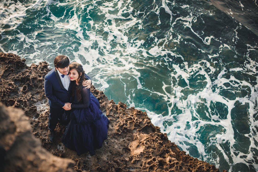 Couple on a cliffside with the bride wearing a flowing cape maxi