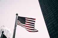 现代摩天大楼背景下，美国国旗在低角度视图中飘扬