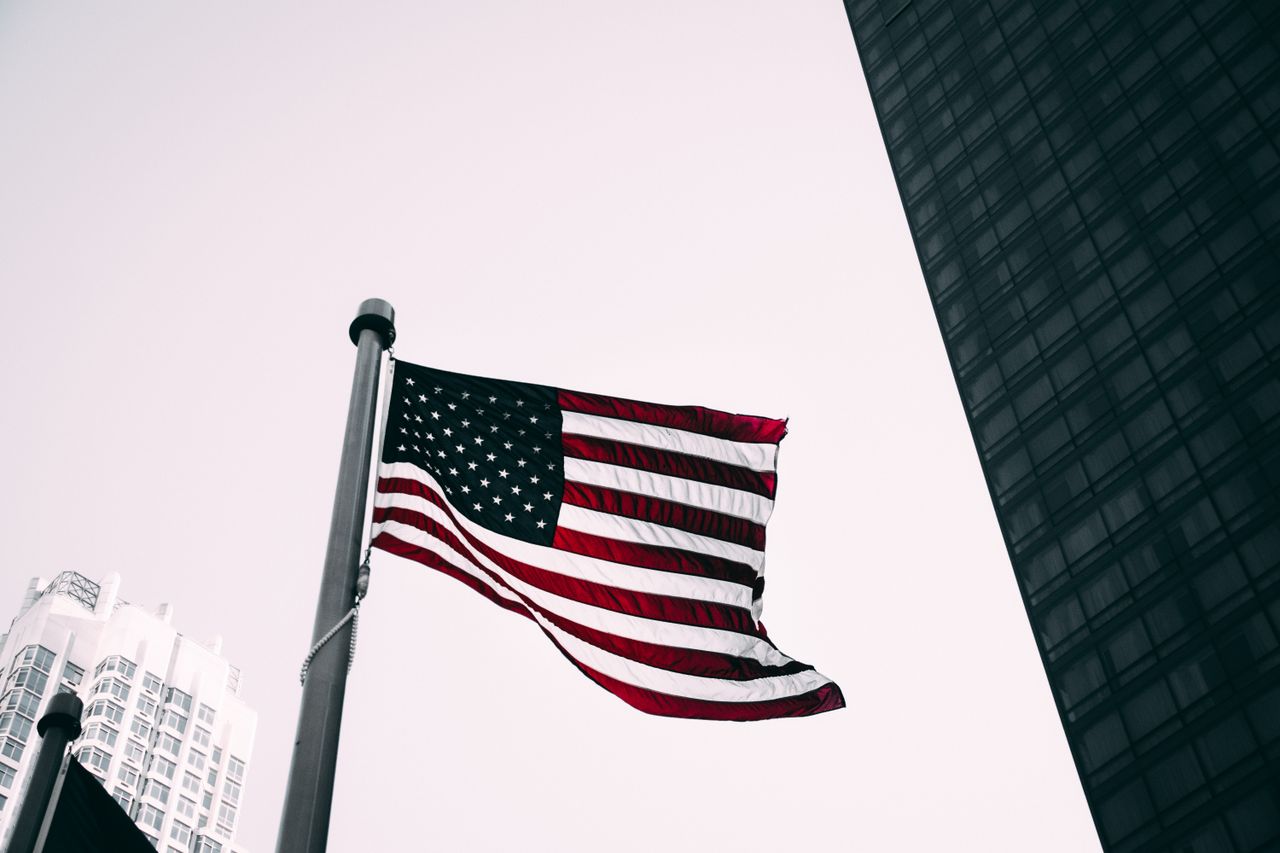 low angle view of the american flag waving against modern skyscraper b