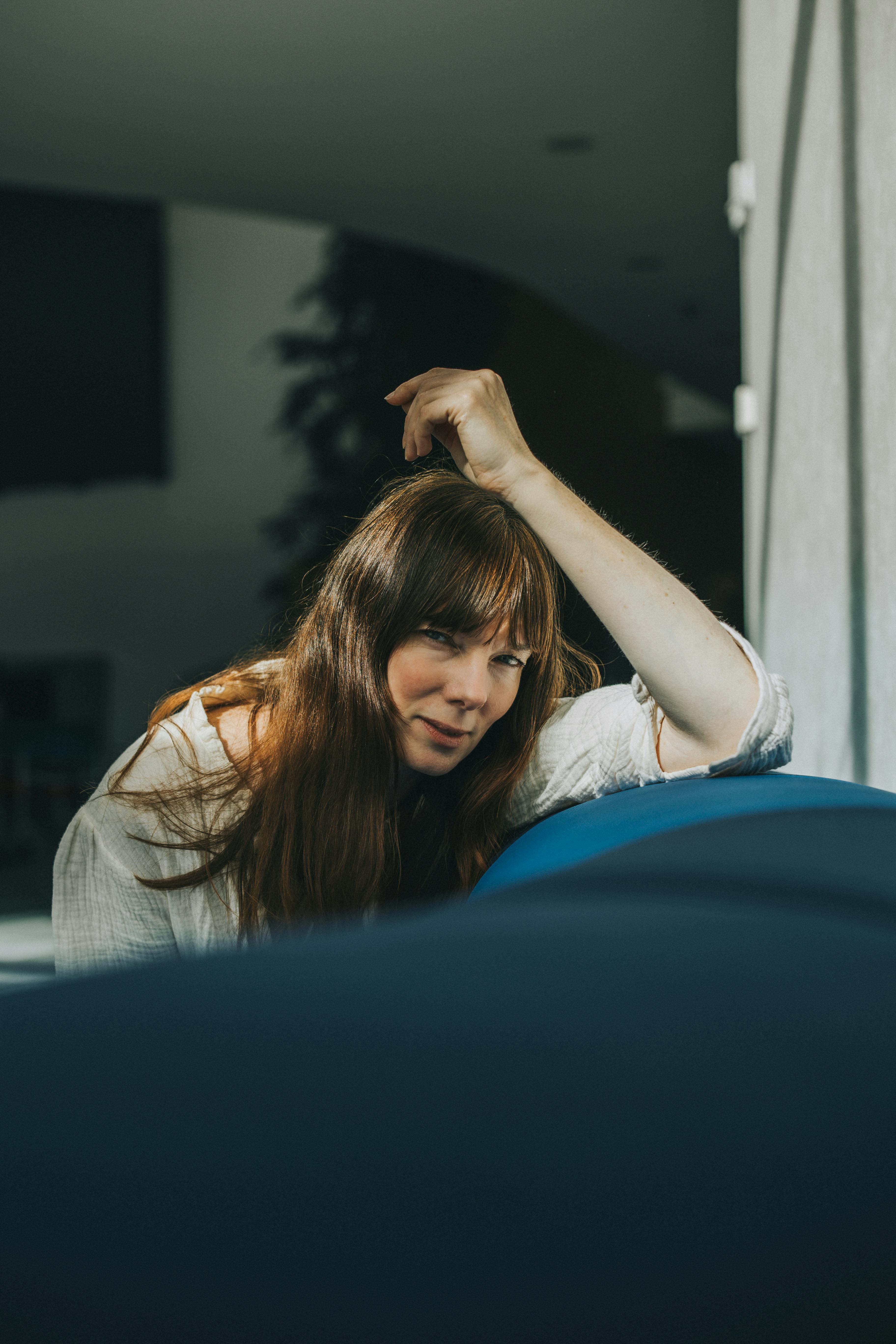 A woman with brown hair sitting casually on a blue couch in warm lighting.