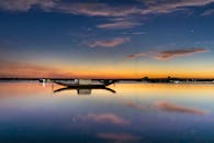 在宁静的日落时分，一艘船的剪影倒映在平静的湖面上，映衬着色彩缤纷的天空