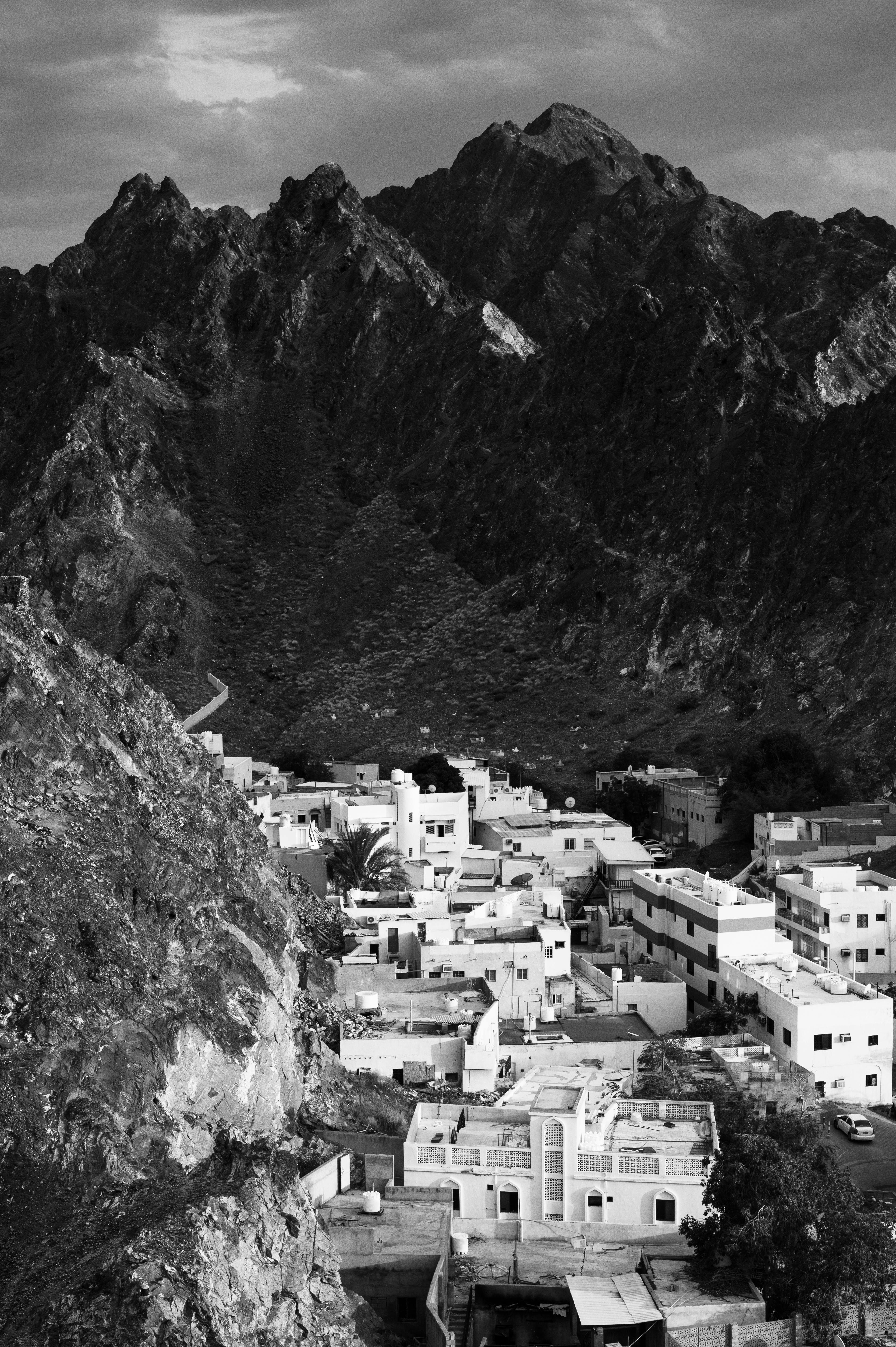 Black and white aerial view of a village in Muscat, Oman with dramatic rocky mountains in the background.