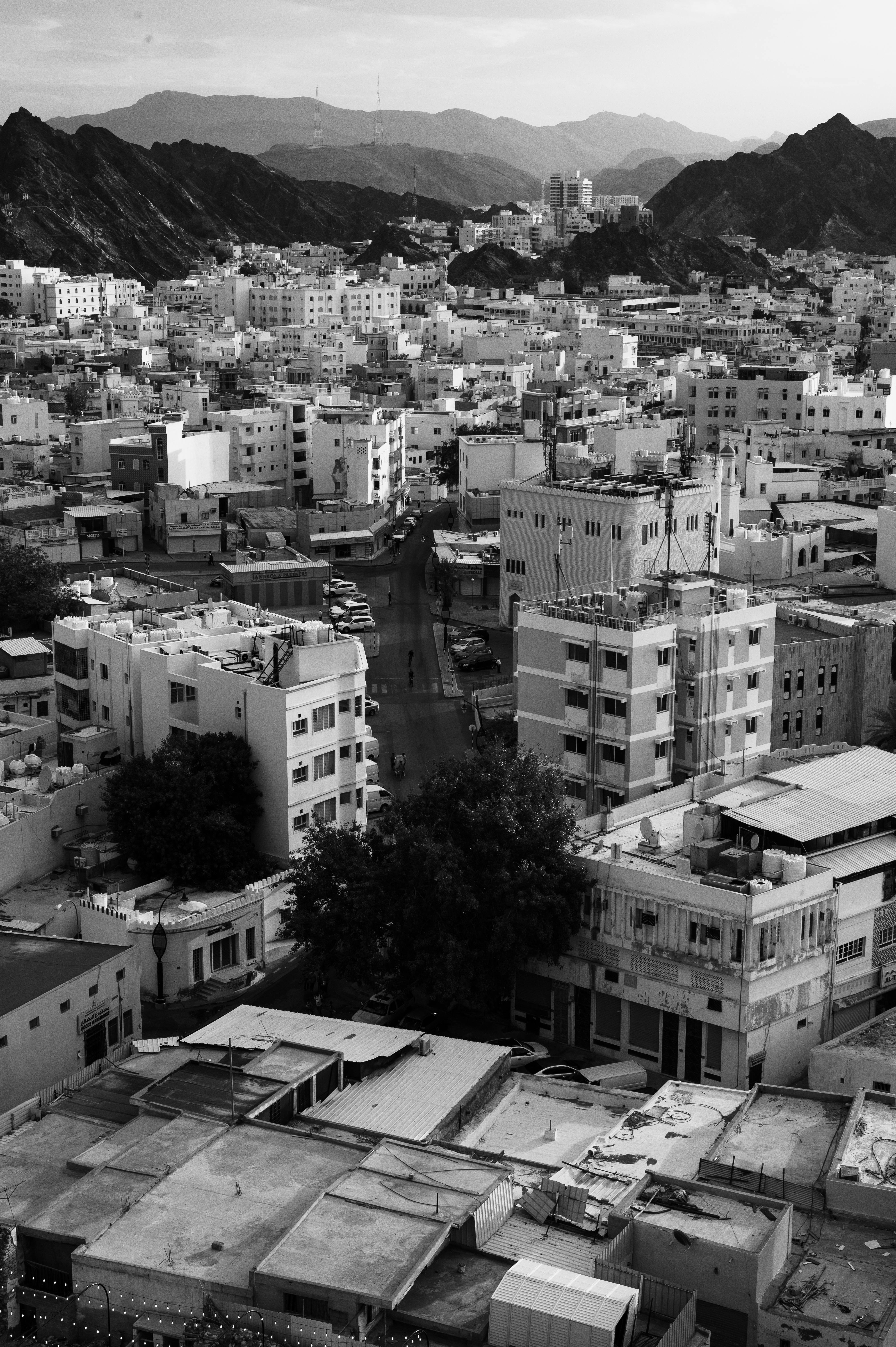 Black and white aerial view of Muscat's urban landscape with distant mountains.