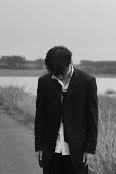 Black and white photo of a man in a suit looking down in a rainy outdoor setting, conveying a somber mood.