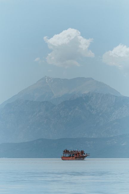 A serene view of a boat sailing with mountains in Antalya, Türkiye.