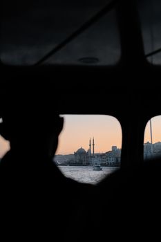 Silhouette of a person looking at Istanbul skyline through a window during sunset.