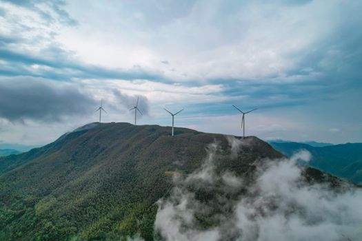 Drone shot capturing wind turbines on a foggy mountain landscape in Jiangxi Province, China.
