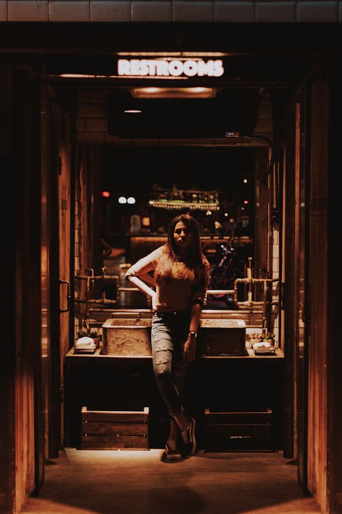 Woman Wearing Denim Jeans Standing Under Restrooms Neon Sign