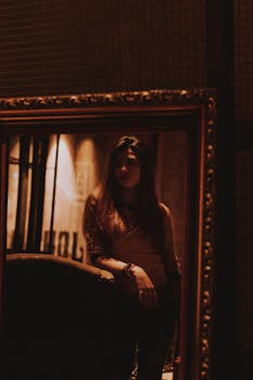 一幅描绘室内女子的肖像画色调幽暗、情绪阴郁，画中人物映照在一面华丽的大镜子里