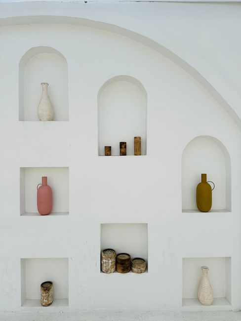 Elegant white wall with minimalist niches showcasing colorful vases in a modern design.