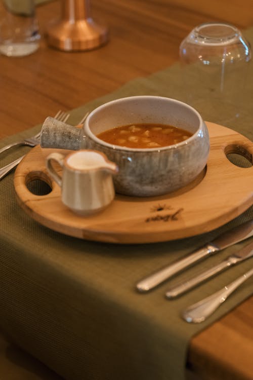 A bowl of soup sits on a wooden tray