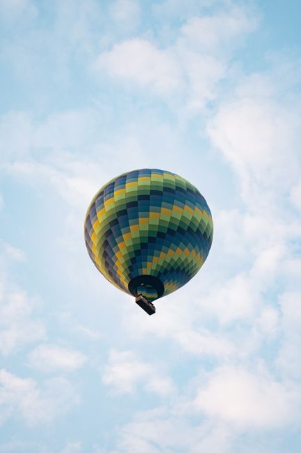 Vibrant hot air balloon floats amidst clouds in Göreme, Türkiye, capturing adventure in a serene sky.