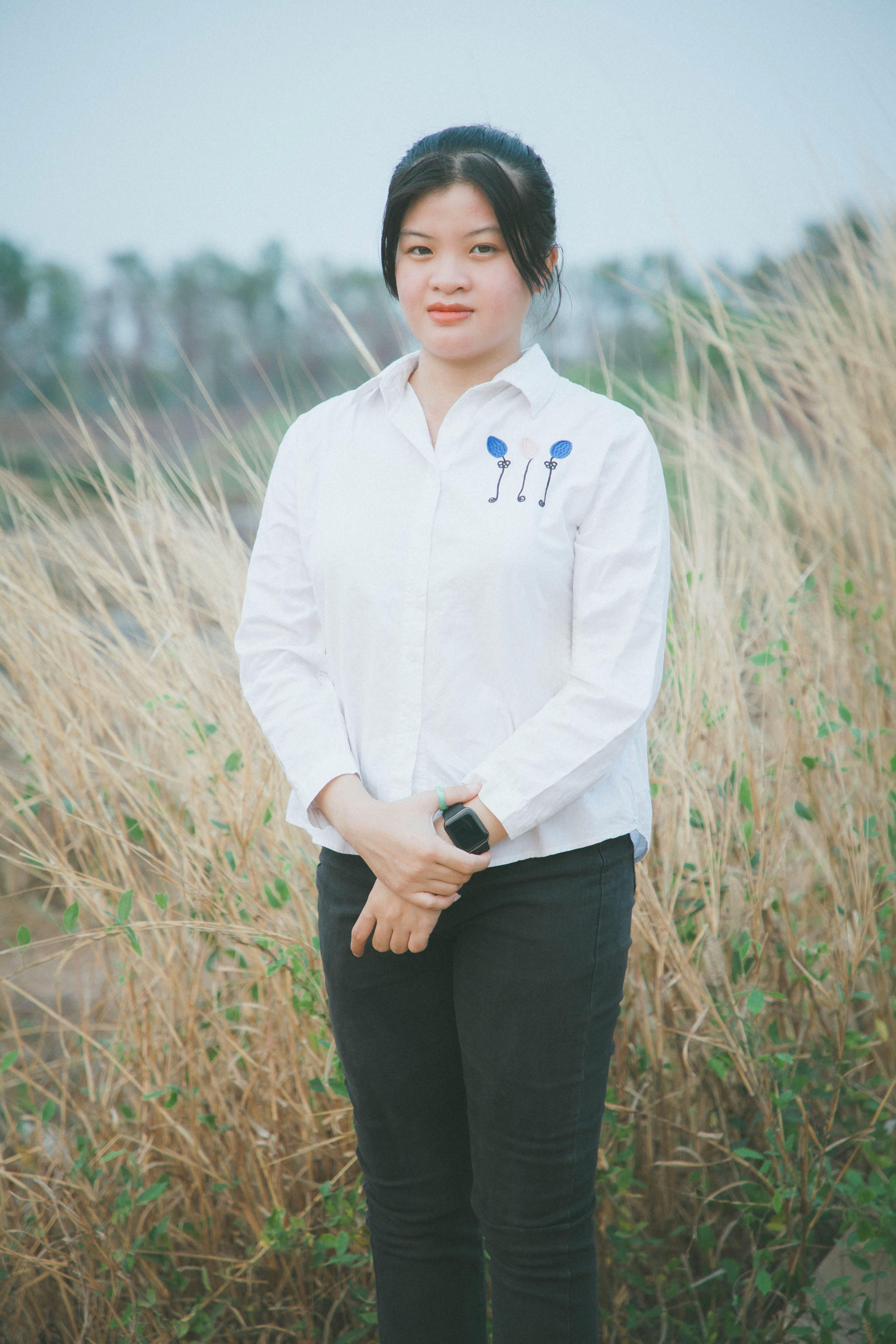 A young woman stands confidently in a grassy rural field wearing casual clothing.