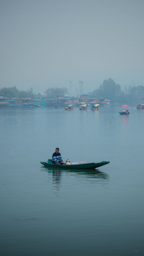 Free A tranquil morning scene with a person on a canoe amidst a foggy lake and distant village. Stock Photo