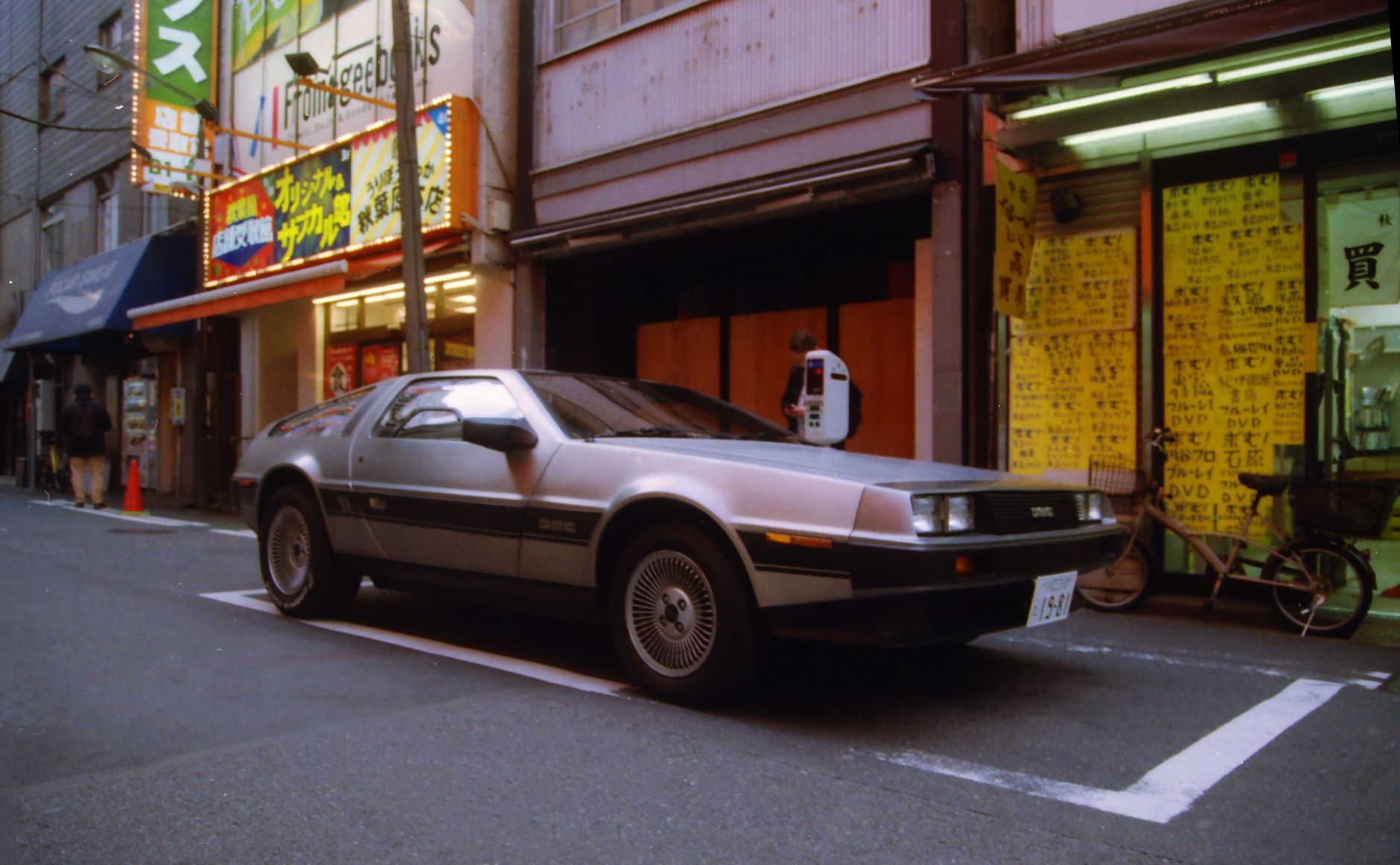 DeLorean DMC-12 parked on a neon-lit street in Akihabara, Tokyo, showcasing urban life in Japan.