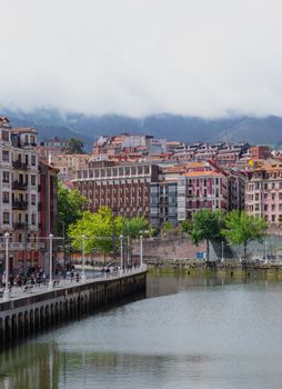 A vibrant view of Bilbao's architecture and riverbanks under cloudy skies.