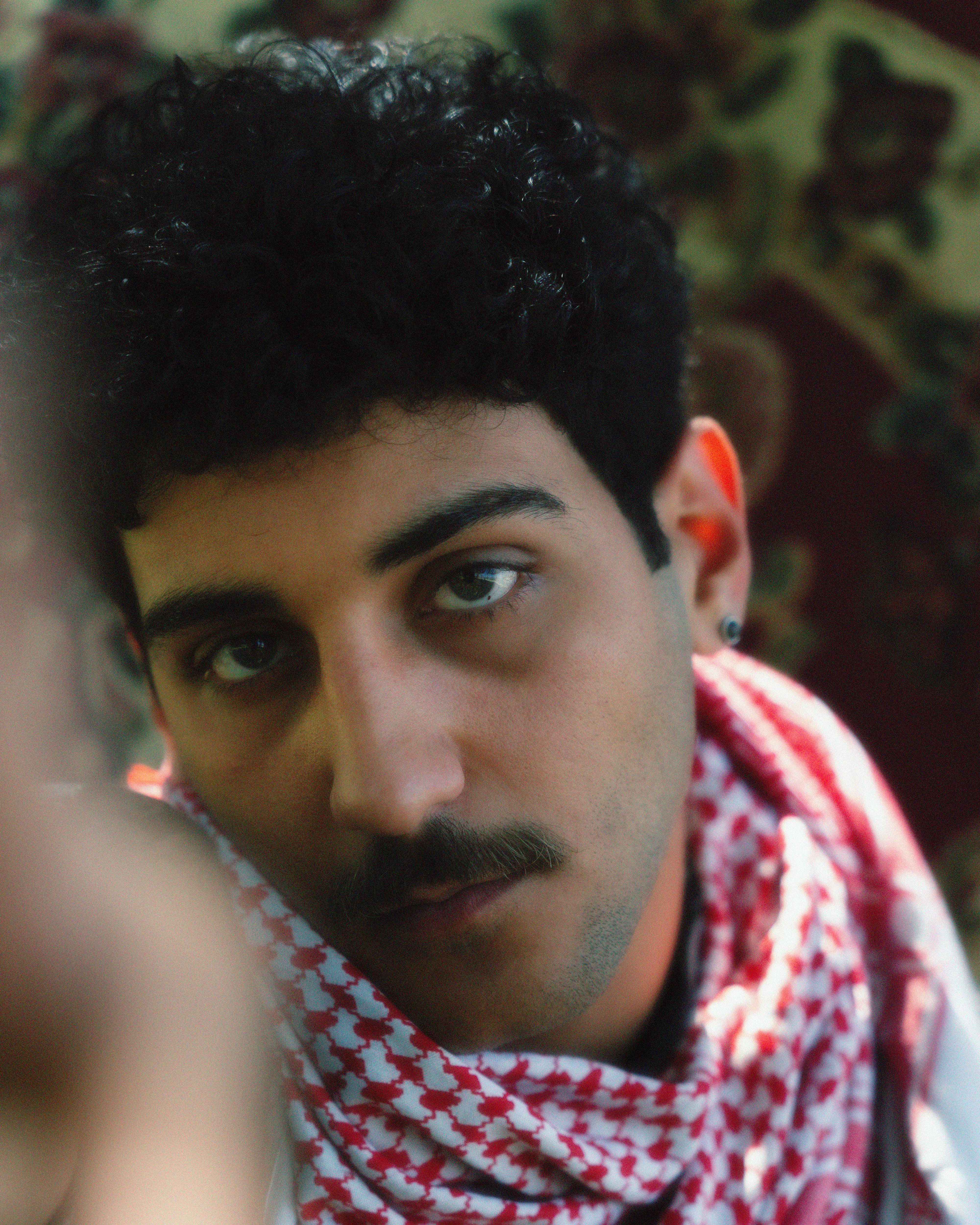 A close-up portrait of a man wearing a red and white patterned scarf outdoors.
