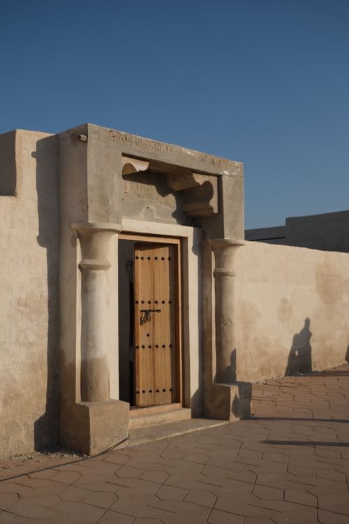 Free A vintage wooden door framed by stone columns under a clear blue sky, casting shadows. Stock Photo