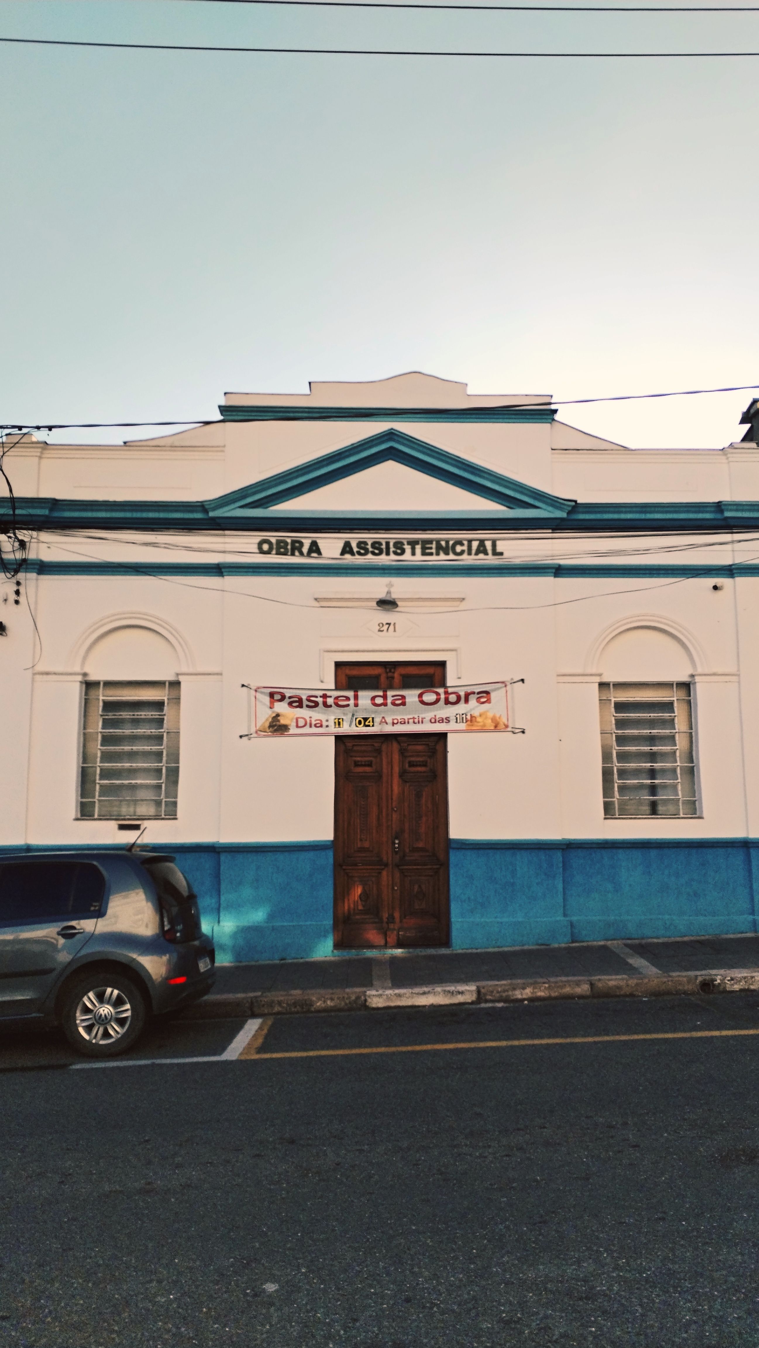 Front view of a historic urban building with blue accents and a sign advertising a local event.