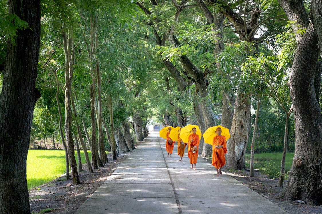 Four Person Walking Under Yellow Umbrellas