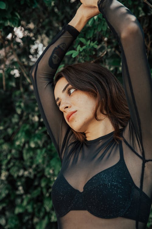 A woman in a sheer bodysuit posing in front of a tree