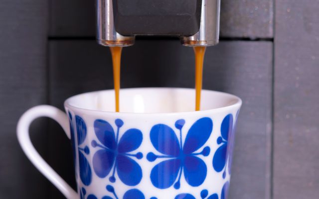 Twin streams of coffee pouring from a Philips bean-to-cup spout into a blue and white patterned cup