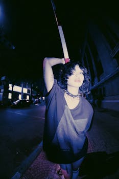 Artistic urban night portrait of a woman standing with arm raised, wearing a t-shirt.