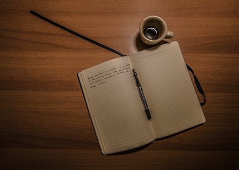 Pen on Notebook Beside a Teacup on Brown Wooden Plank