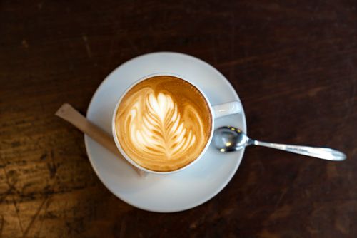 Free Top-down image of a cappuccino with latte art on a wooden table, served with spoon and sugar. Stock Photo