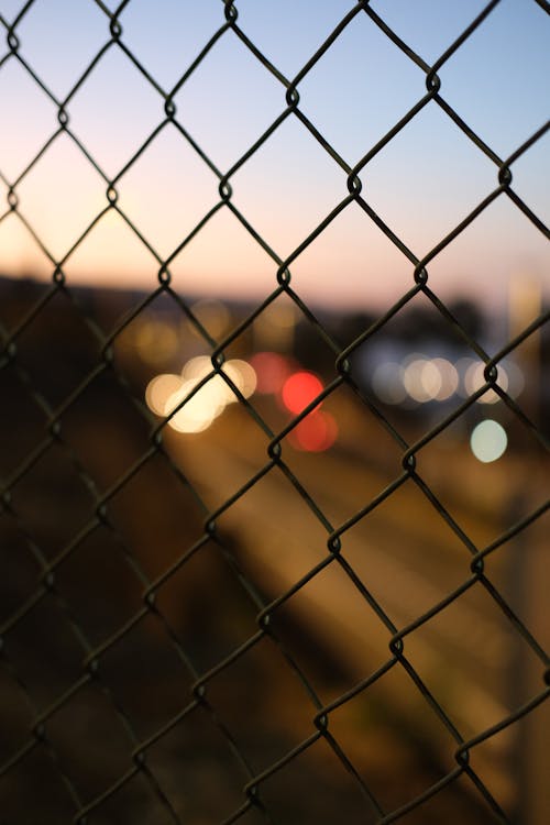 Close-up of a Chain Fence and Blurry City Lights in the Background at Sunset