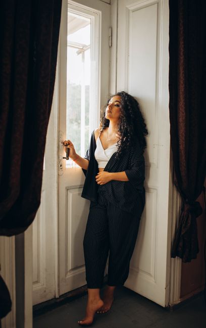 A woman in casual attire standing barefoot by a sunlit doorway, gazing outside.