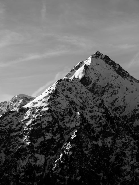 A dramatic black and white image of snowcapped mountain peaks under a clear sky.