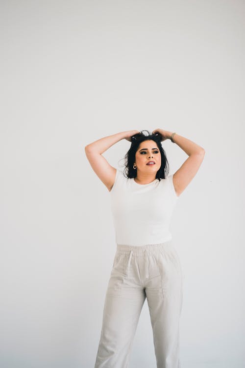 A woman in white top and pants standing in front of a white wall