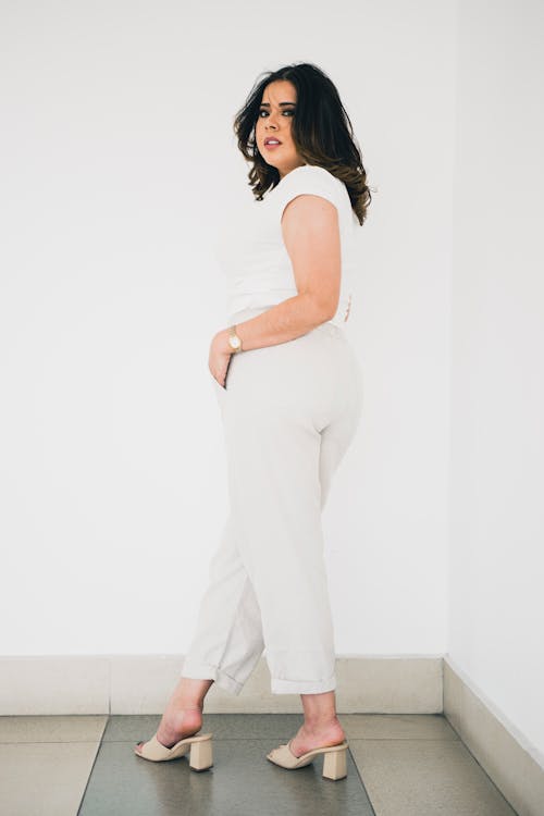 A woman in a white top and pants standing in front of a white wall