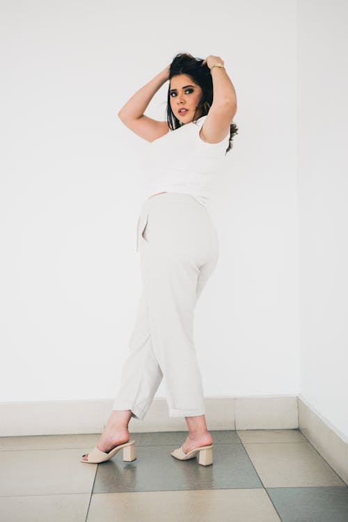 A woman in white pants and heels posing for a photo