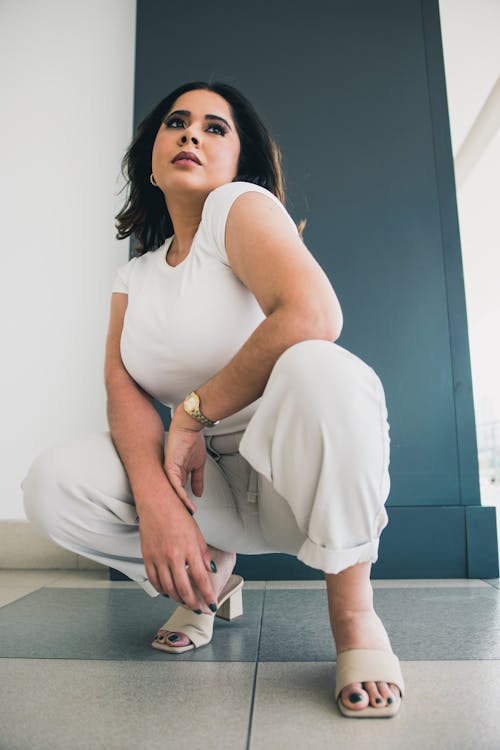 A woman in white pants crouches down on the floor