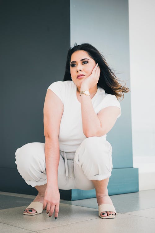 A woman in white pants crouches down and poses for a photo