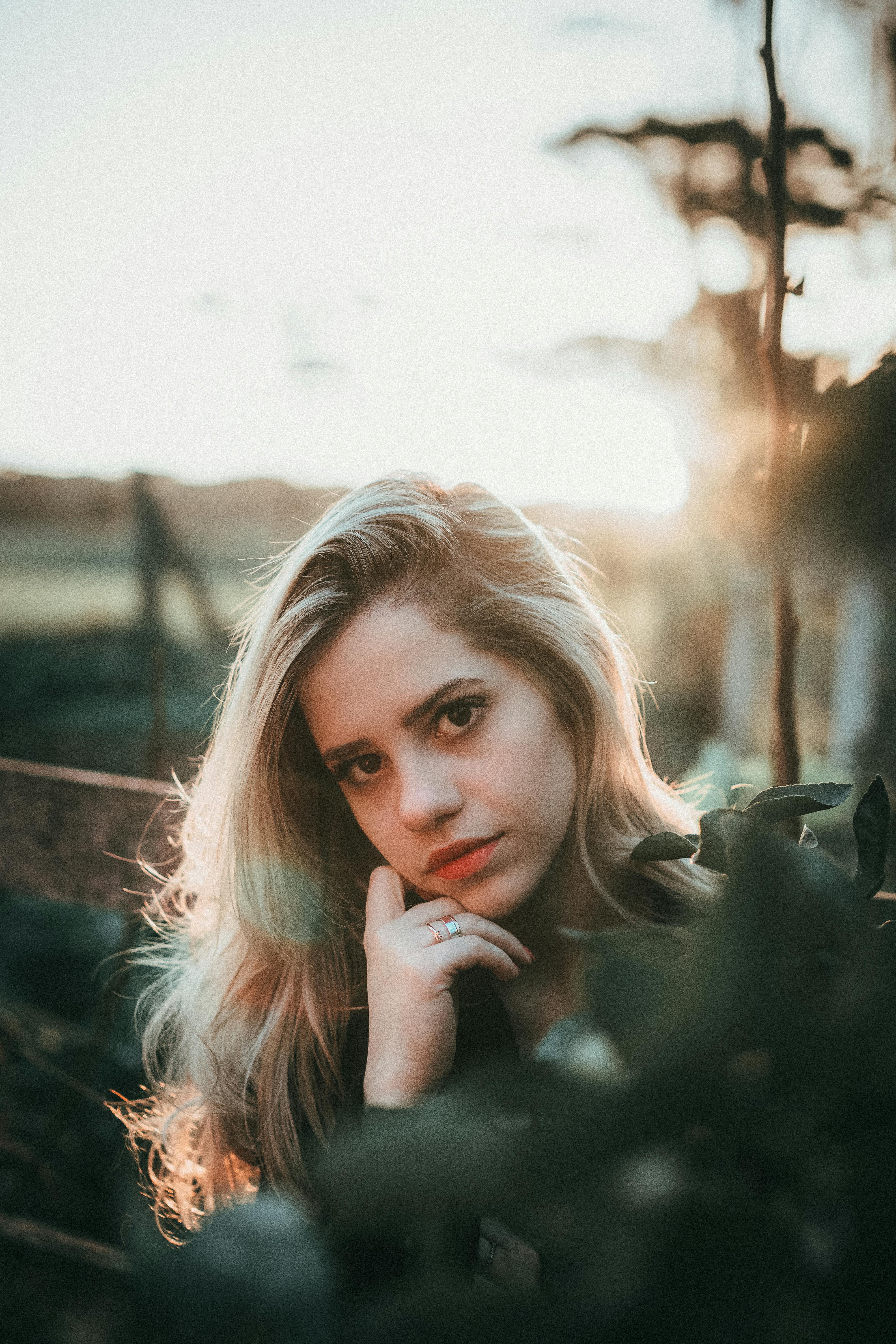 Blonde woman posing outdoors in natural light during golden hour, surrounded by greenery.