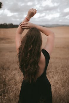 Back view of a woman in a black dress posing in a golden wheat field.