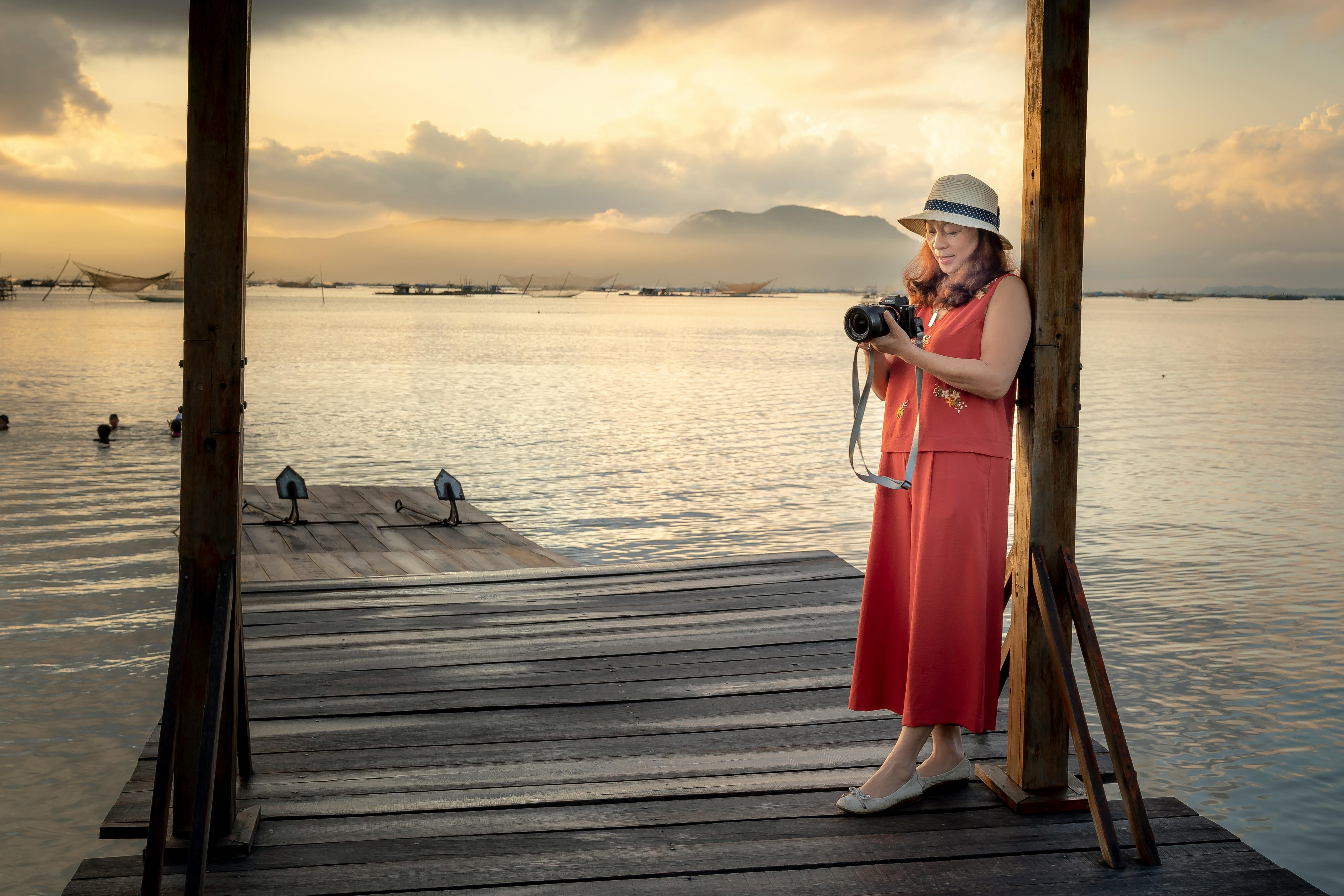 日落时分，一位女摄影师站在湖边宁静的码头上，捕捉着眼前的景象