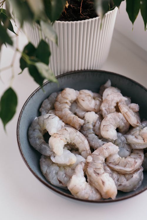 A bowl of shrimp sitting on a table next to a plant