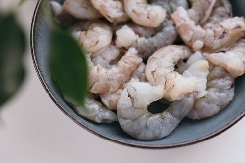 A bowl of shrimp with leaves and a white plant