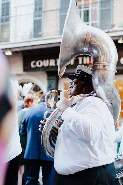 Man in White Shirt and a Cap Playing the Tuba on a Street