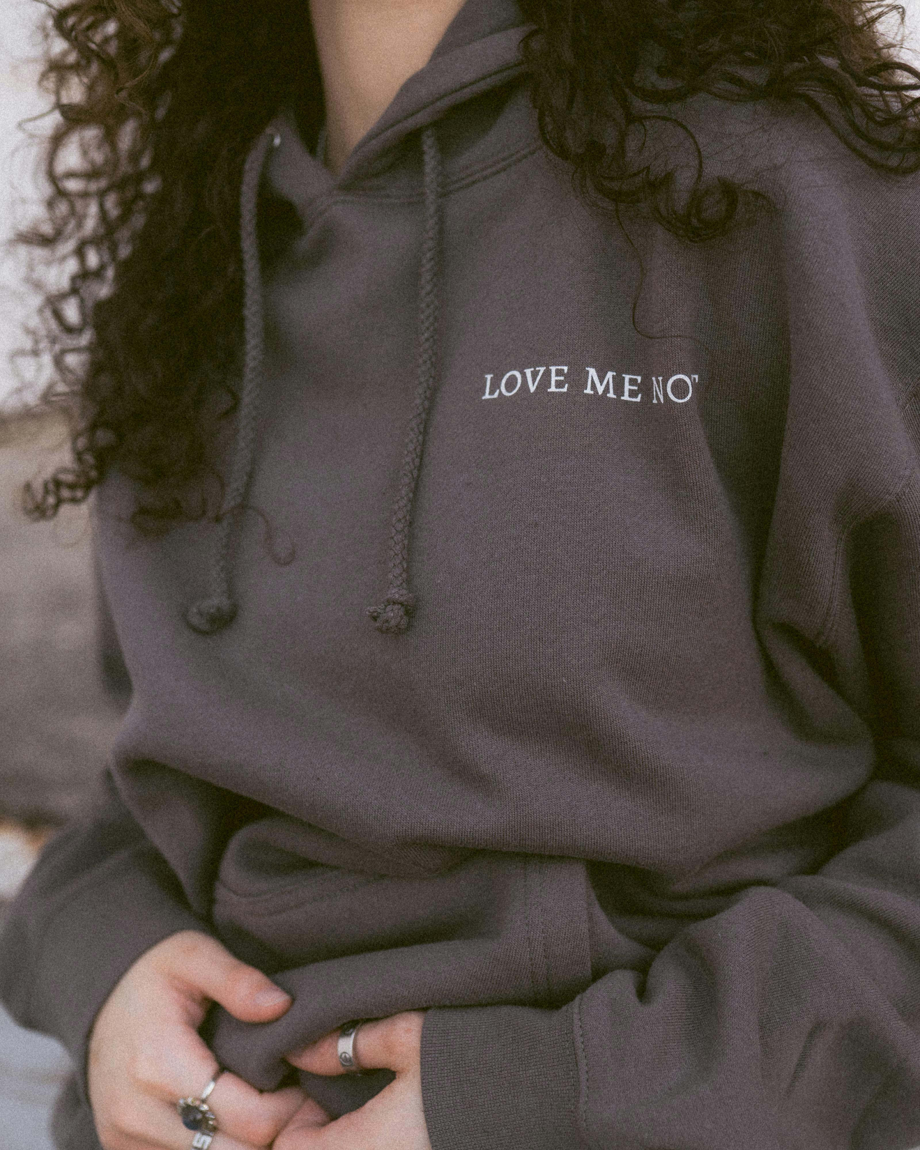 Fashion photo of a woman in a gray hoodie with curly hair and rings, conveying relaxed style.
