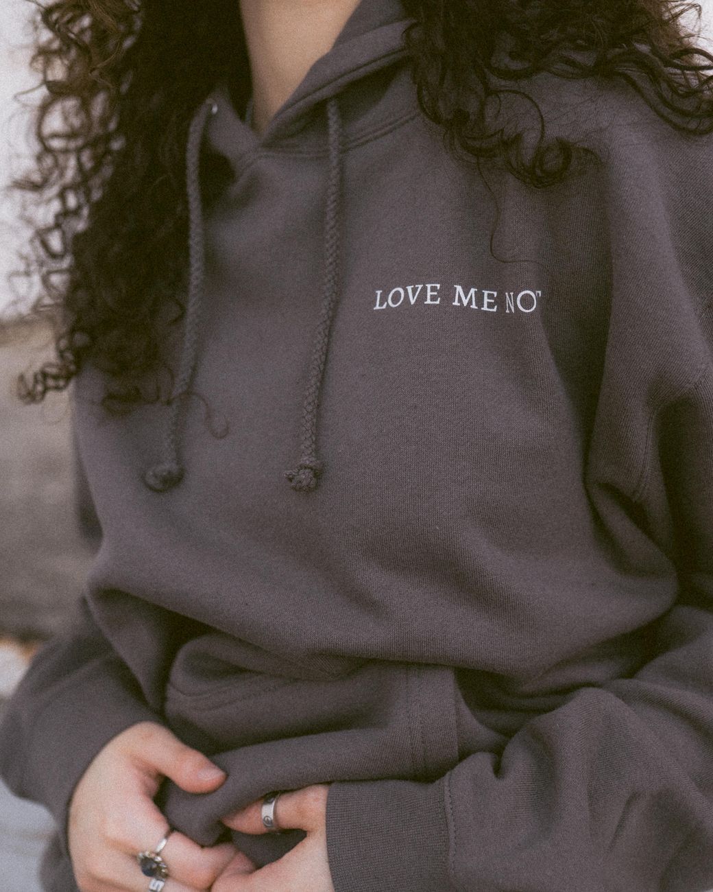 Fashion photo of a woman in a gray hoodie with curly hair and rings, conveying relaxed style.