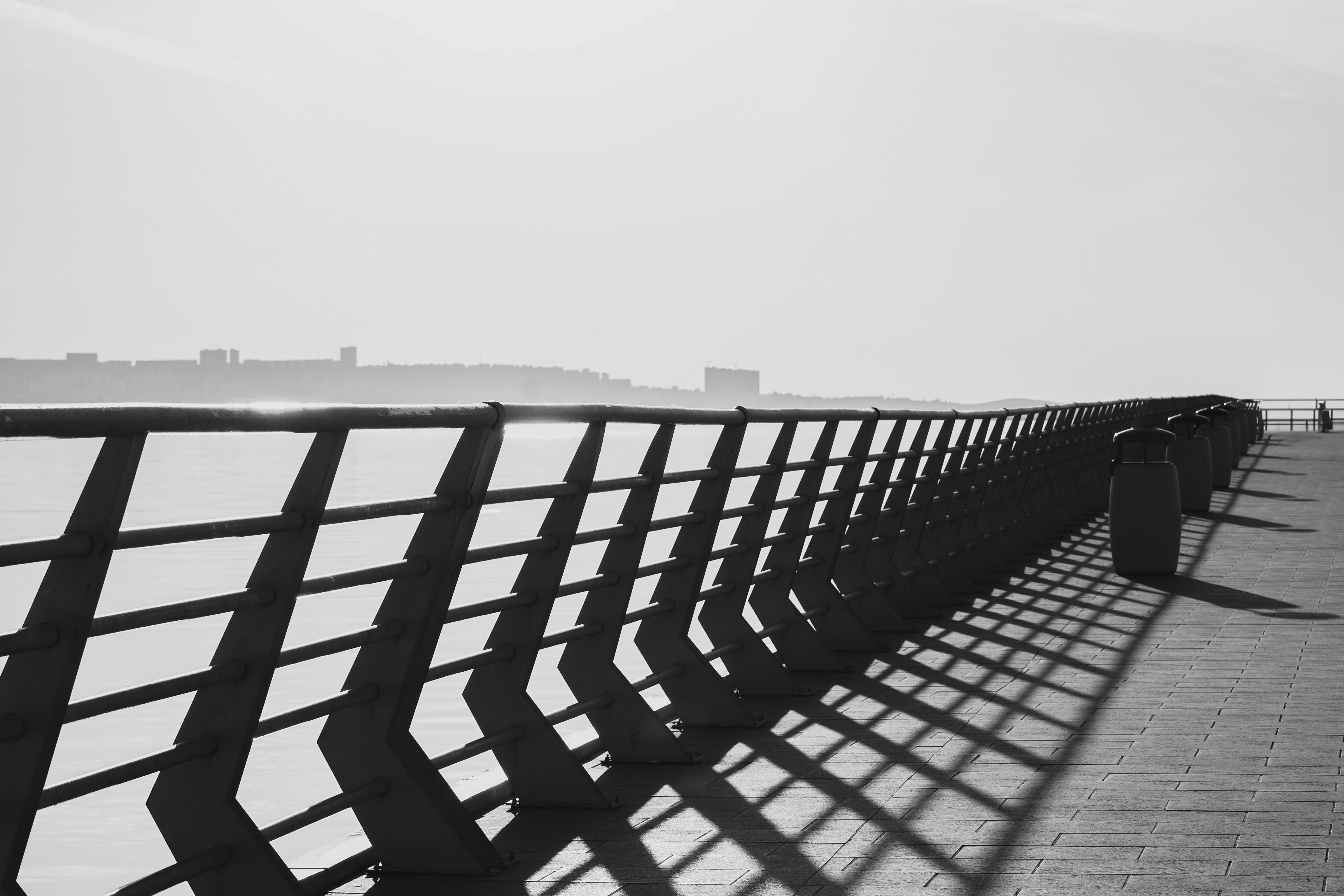 Black and white photo of a sunlit pier casting geometric shadows along the sea.